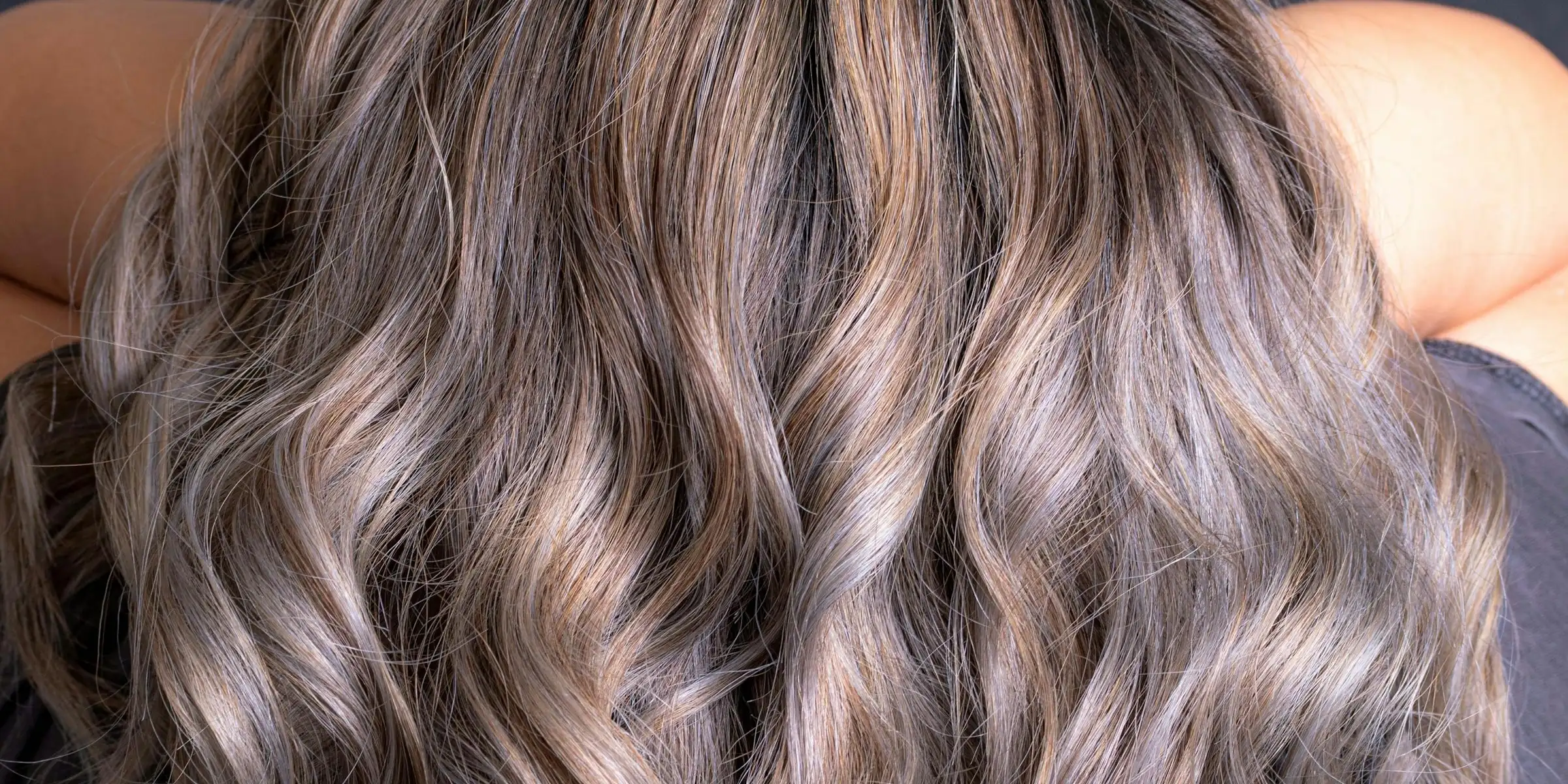 Long, loose waves seen from behind, soft ash-blonde balayage over darker roots