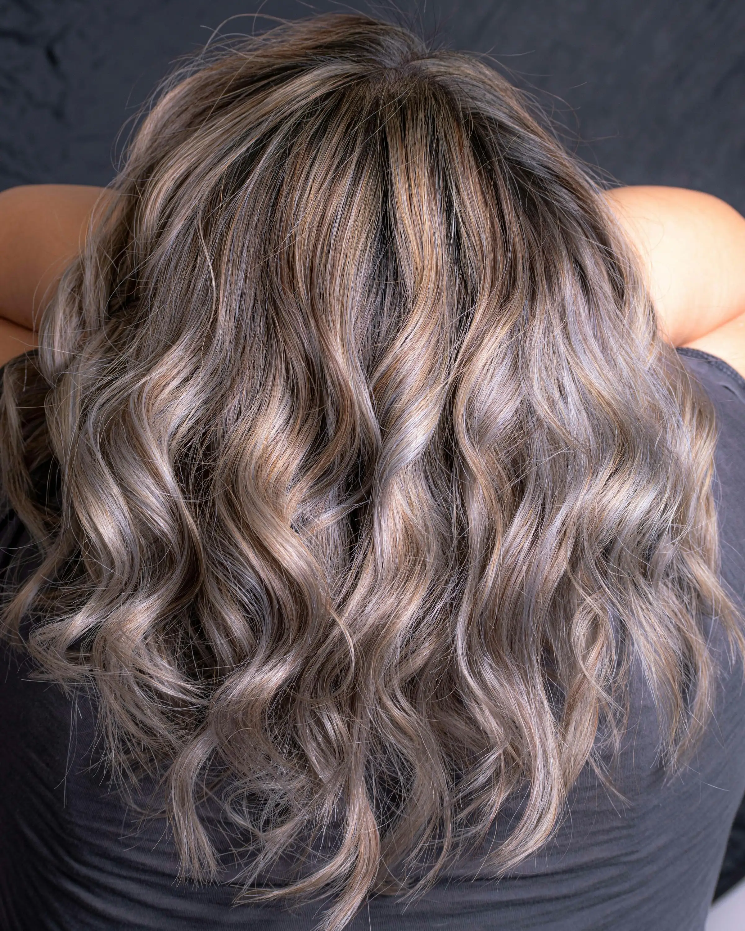 Long, loose waves seen from behind, soft ash-blonde balayage over darker roots