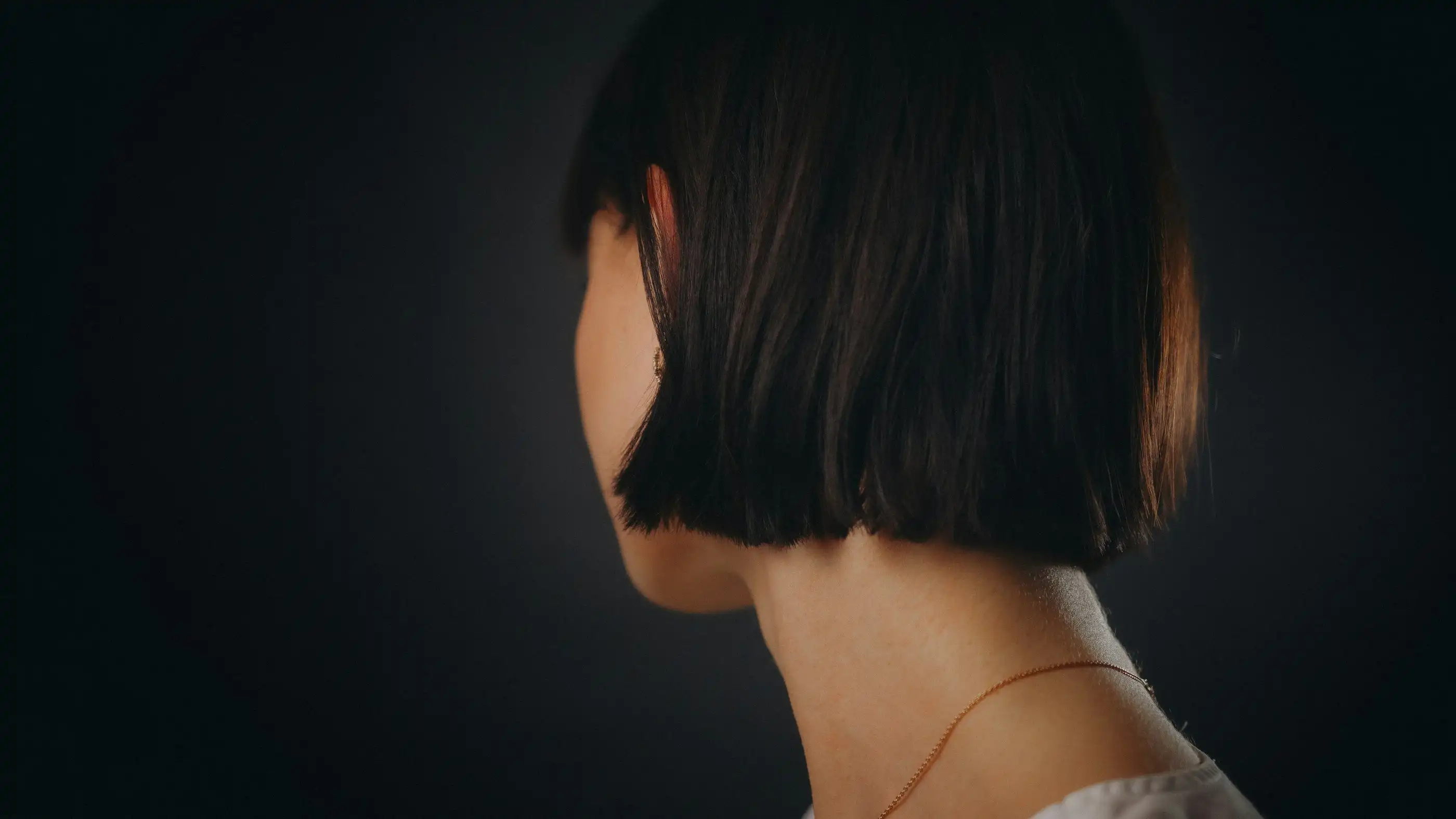 A sleek, chin-length black bob seen from behind against a dark background