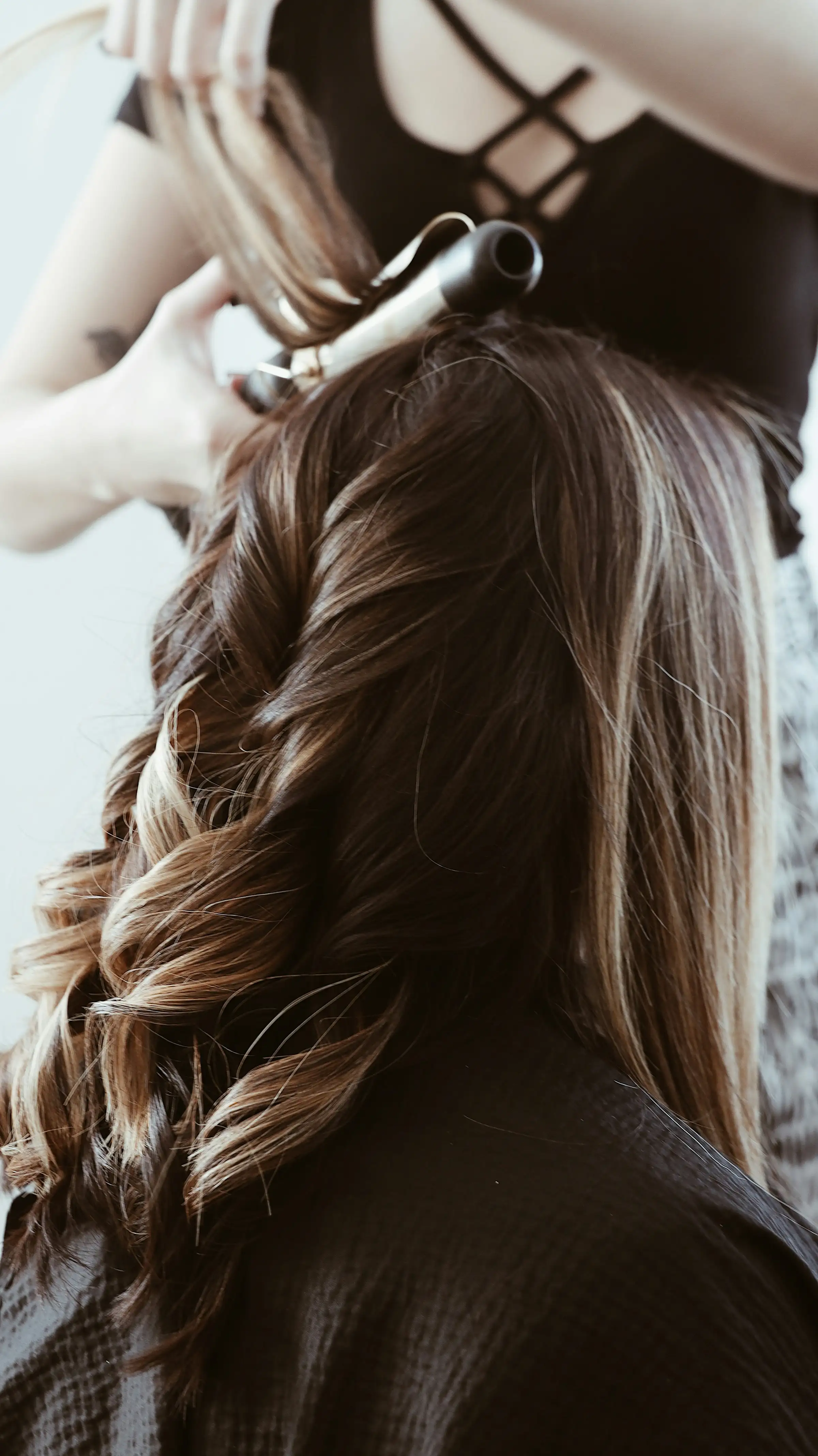 A stylist curling long brunette hair with a curling wand
