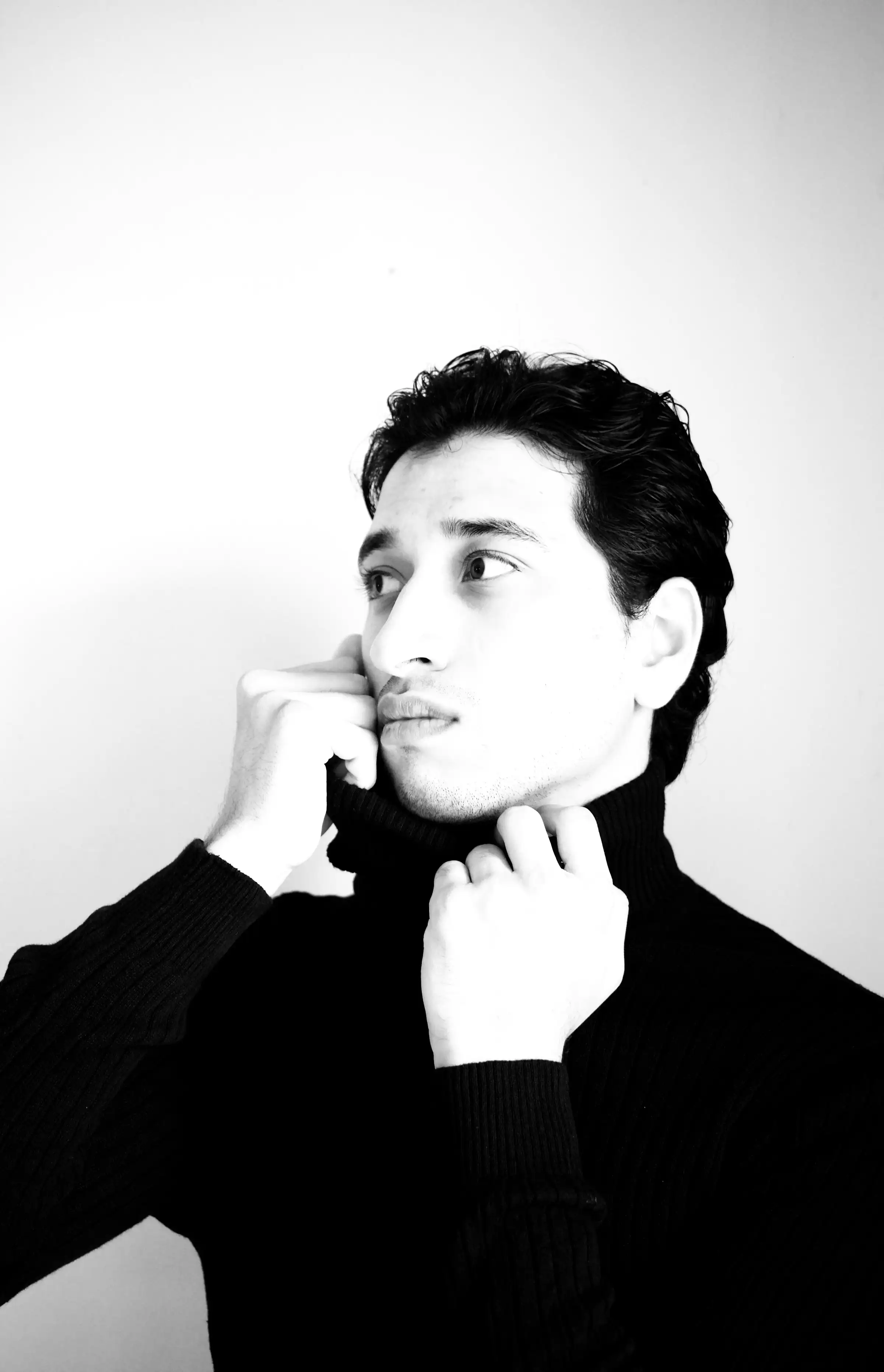 A man with thick dark hair in a black roll-neck, one hand at his collar