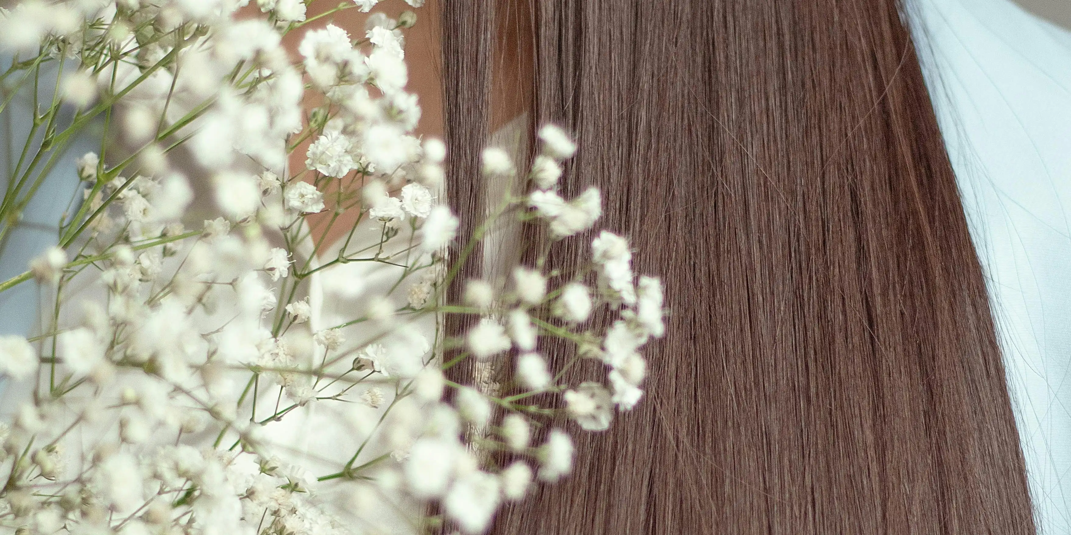 Long, sleek, straight brunette hair beside a spray of white gypsophila