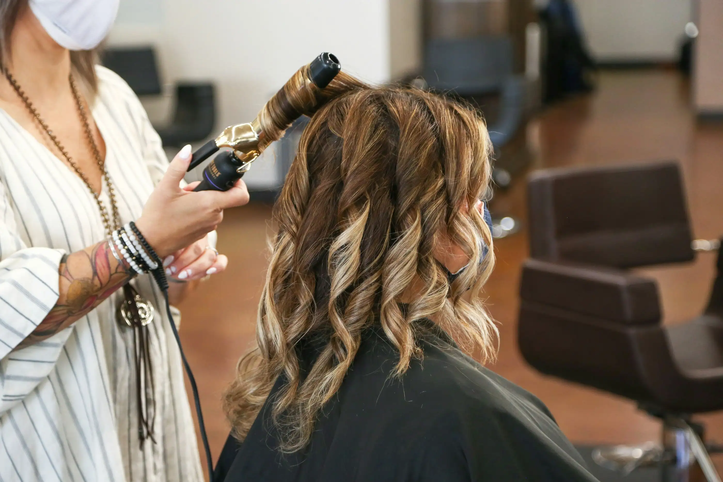 A stylist curling a client's long hair with a curling wand in a salon